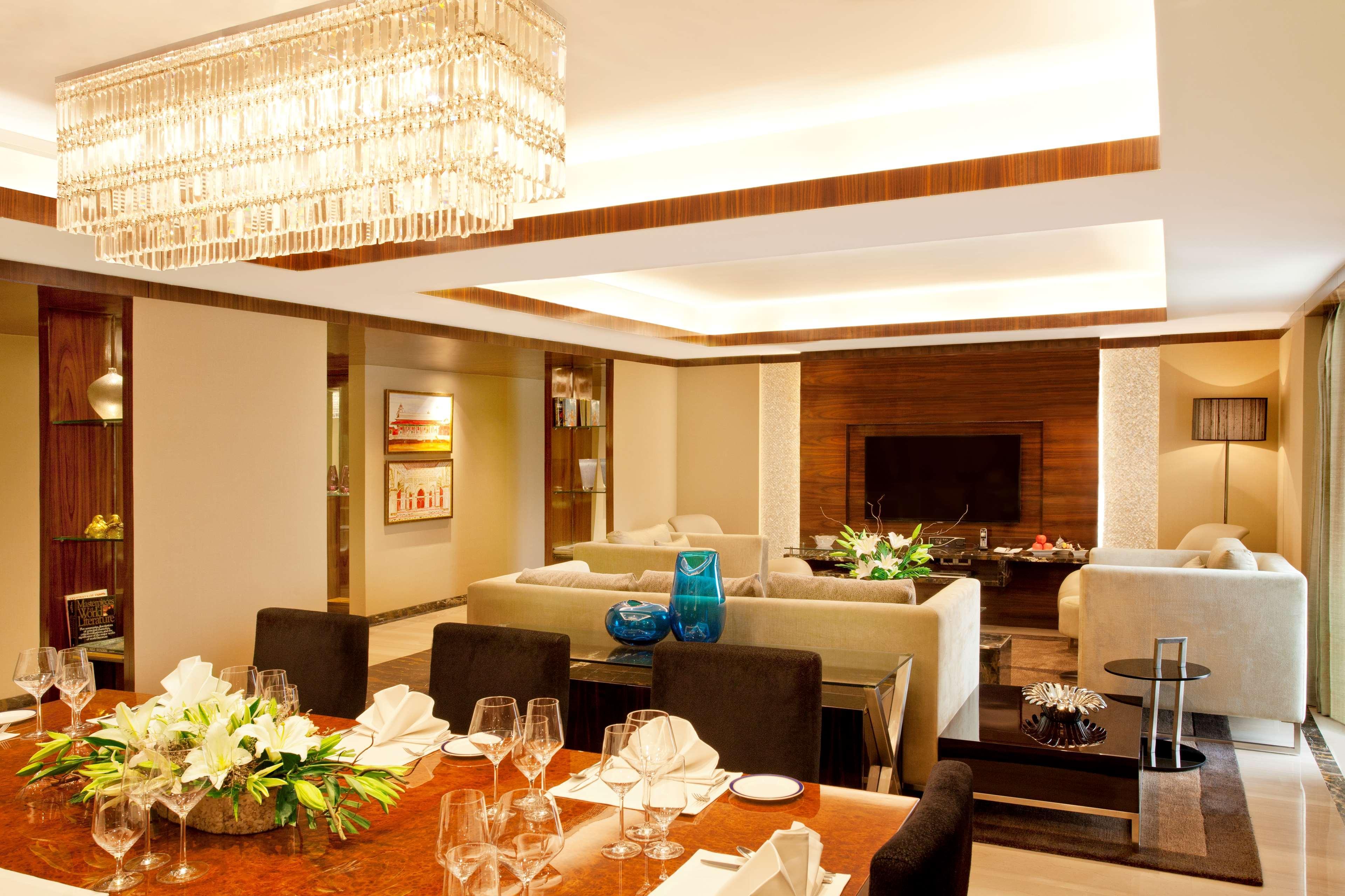 ホテル ラディソン ブルー プラザ デリー エアポート ニューデリー エクステリア 写真 The photo shows a modern and elegantly designed dining area that seamlessly blends with a living space. In the foreground, there is a polished wooden dining table set with elegant tableware, including wine glasses and folded napkins. 

In the backgro